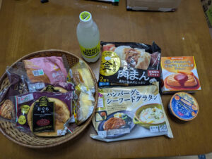 木製テーブルの上に、籠に入った調理済み食品、飲料、冷凍食品、缶詰など複数の市販食品が並んでいる様子